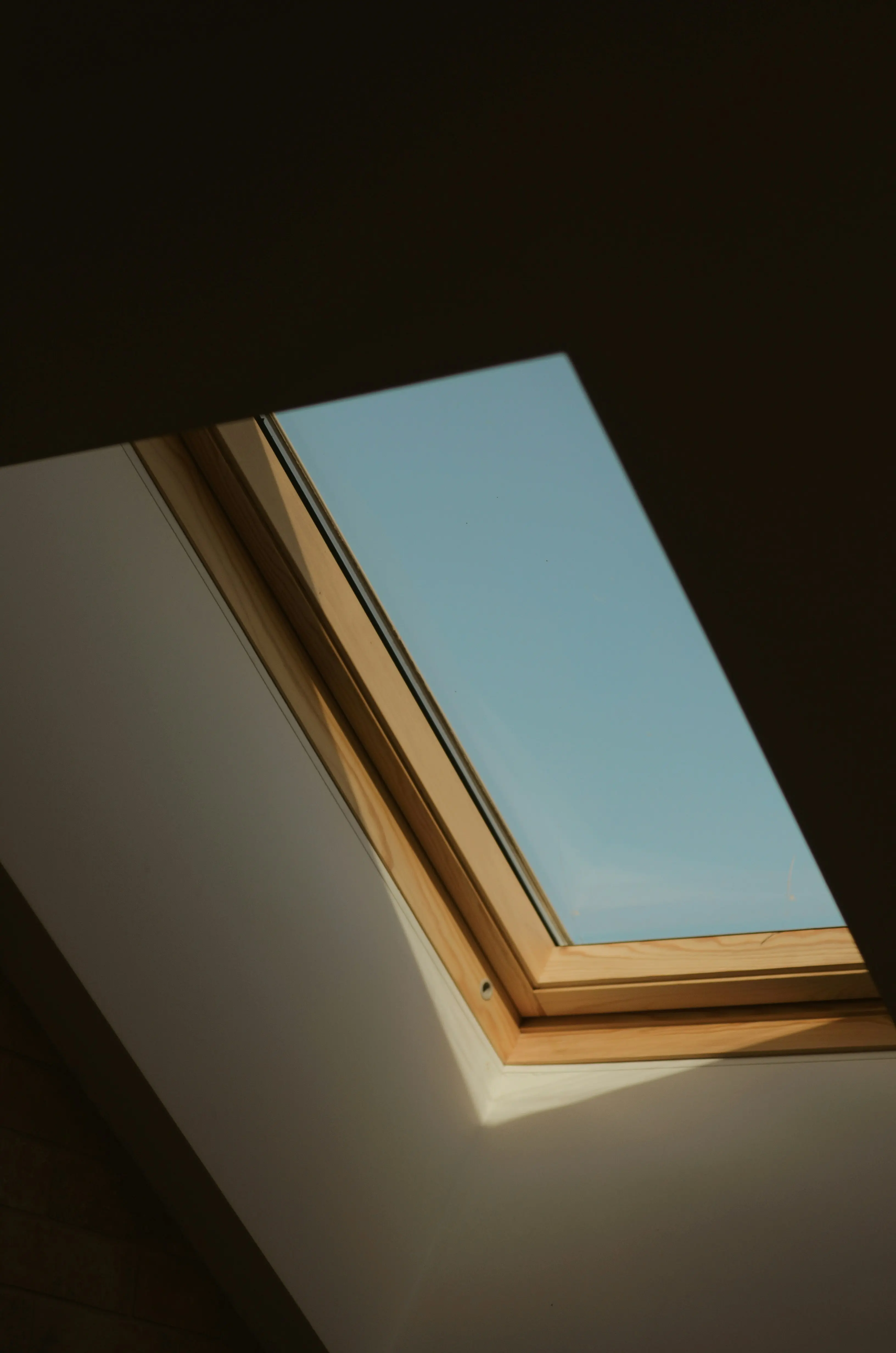 Vue en contre-plongée d'une fenêtre de toit en bois ouverte laissant apparaître un ciel bleu dégagé.