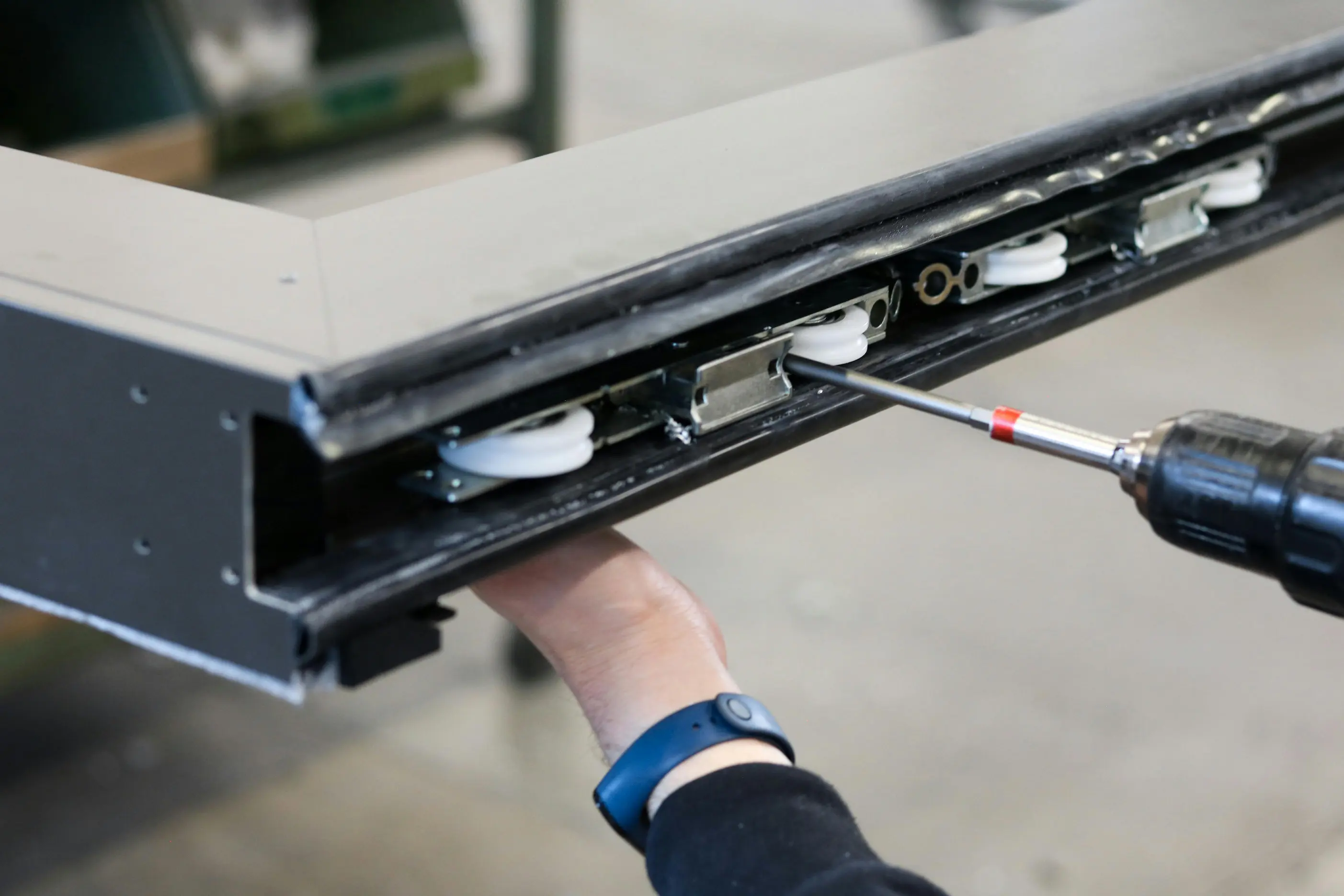 Gros plan sur l'assemblage d'un profilé de fenêtre en atelier, main tenant une visseuse électrique pour fixer la ferrure.