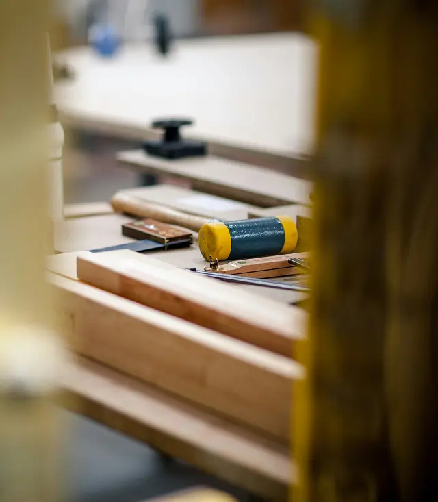Établi d'atelier de menuiserie avec pièces de bois et outils dont un maillet à embouts jaunes, vue en gros plan avec premier plan flou.