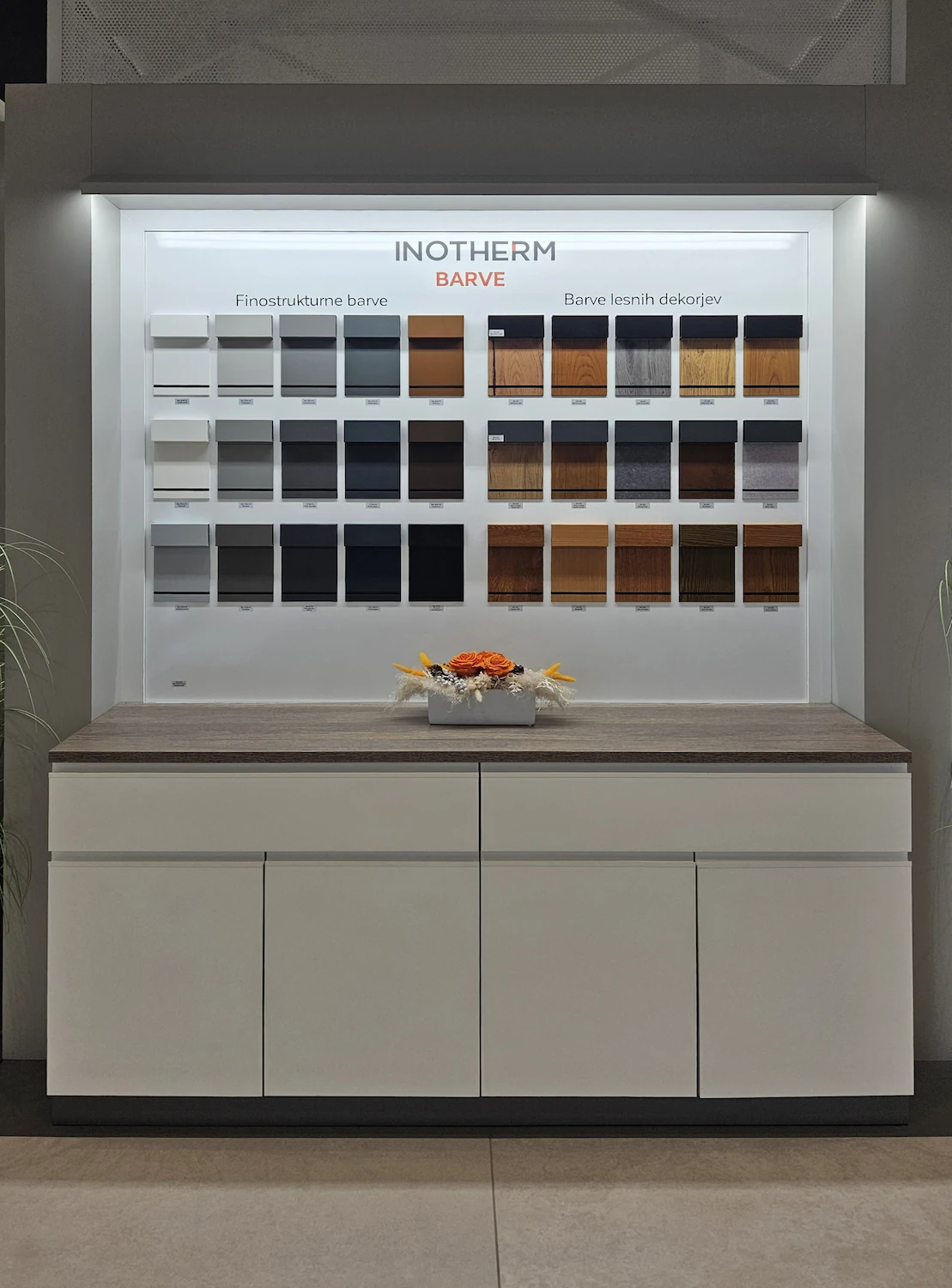 Présentoir showroom Inotherm avec échantillons de teintes de portes d'entrée disposés en grille, au-dessus d'un meuble bas.