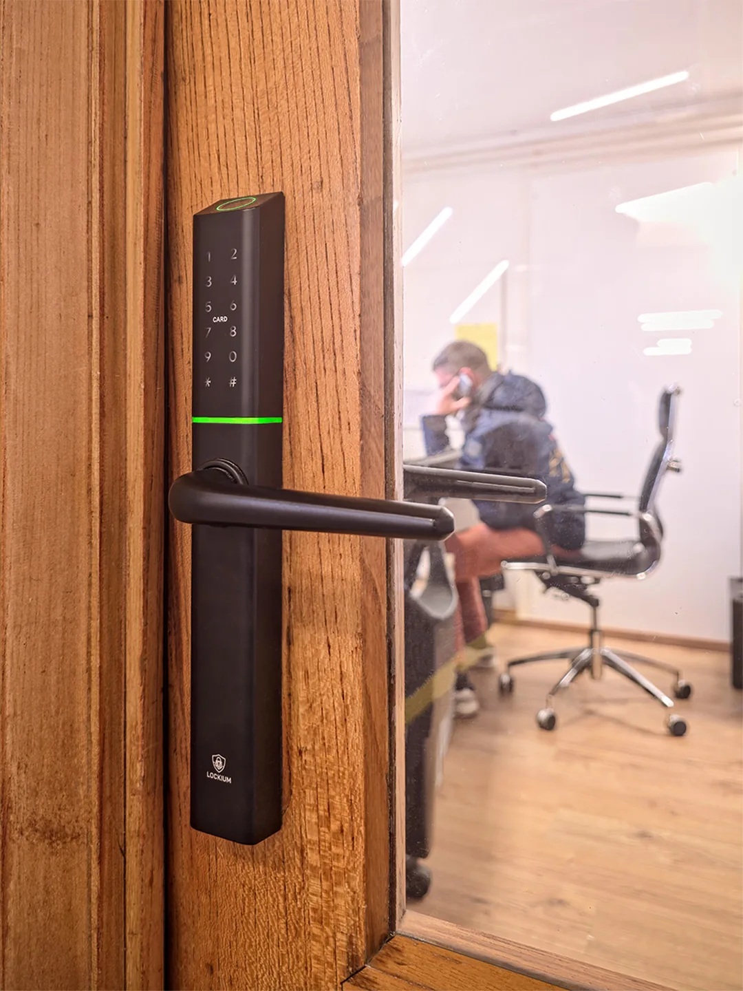 Serrure connectée Lockium noire avec clavier tactile et lecteur d'empreinte digitale, installée sur une porte en bois donnant sur un bureau.