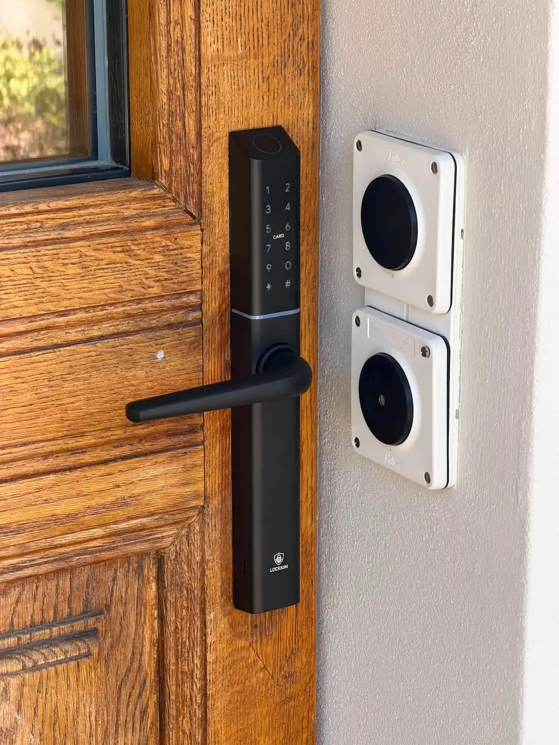 Serrure connectée Lockium noire à clavier tactile et poignée, installée sur une porte d'entrée en bois clair.