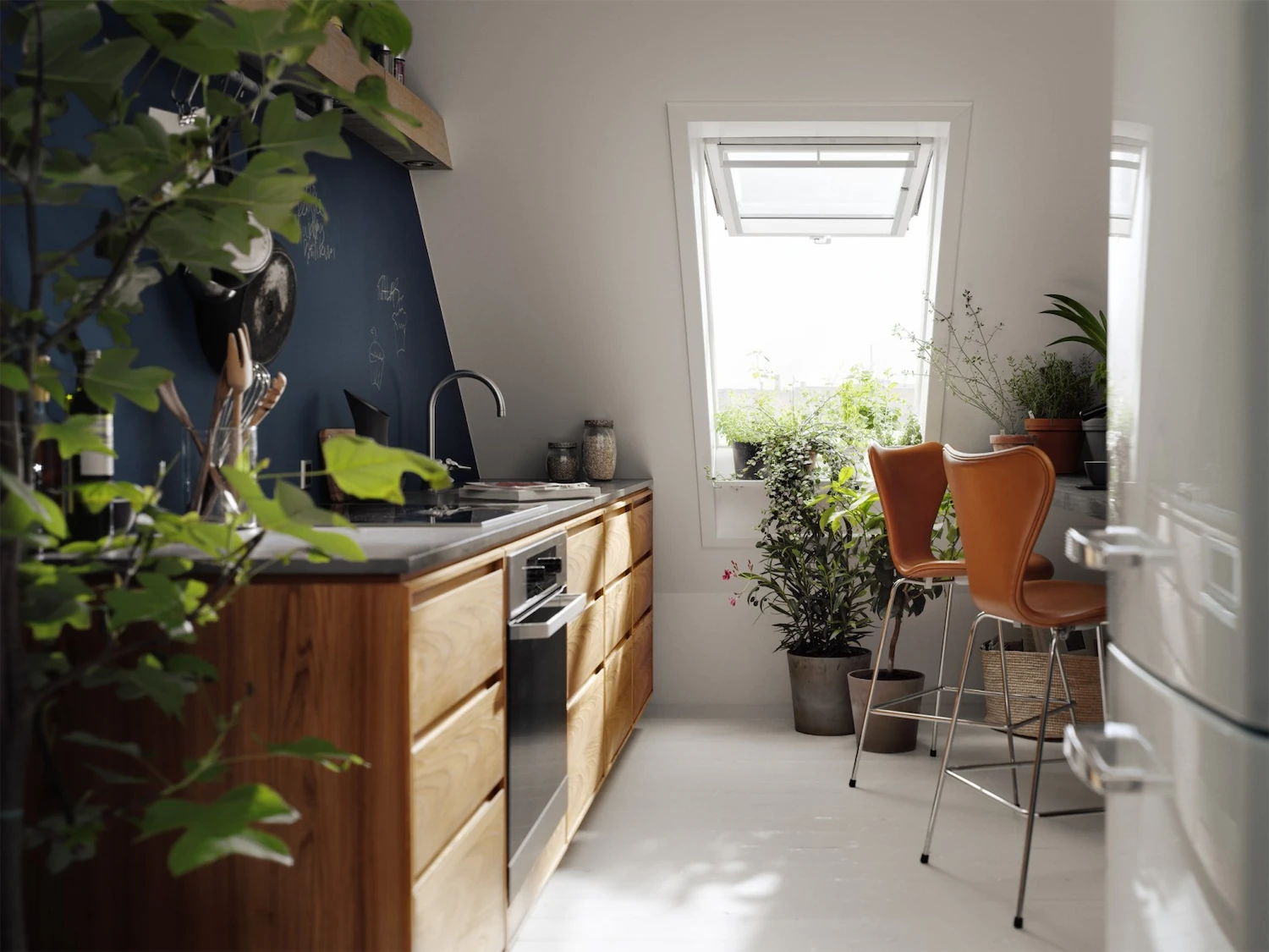 Cuisine sous combles en bois avec fenêtre de toit Velux à projection au-dessus de l'évier, tabourets orange et plantes vertes.