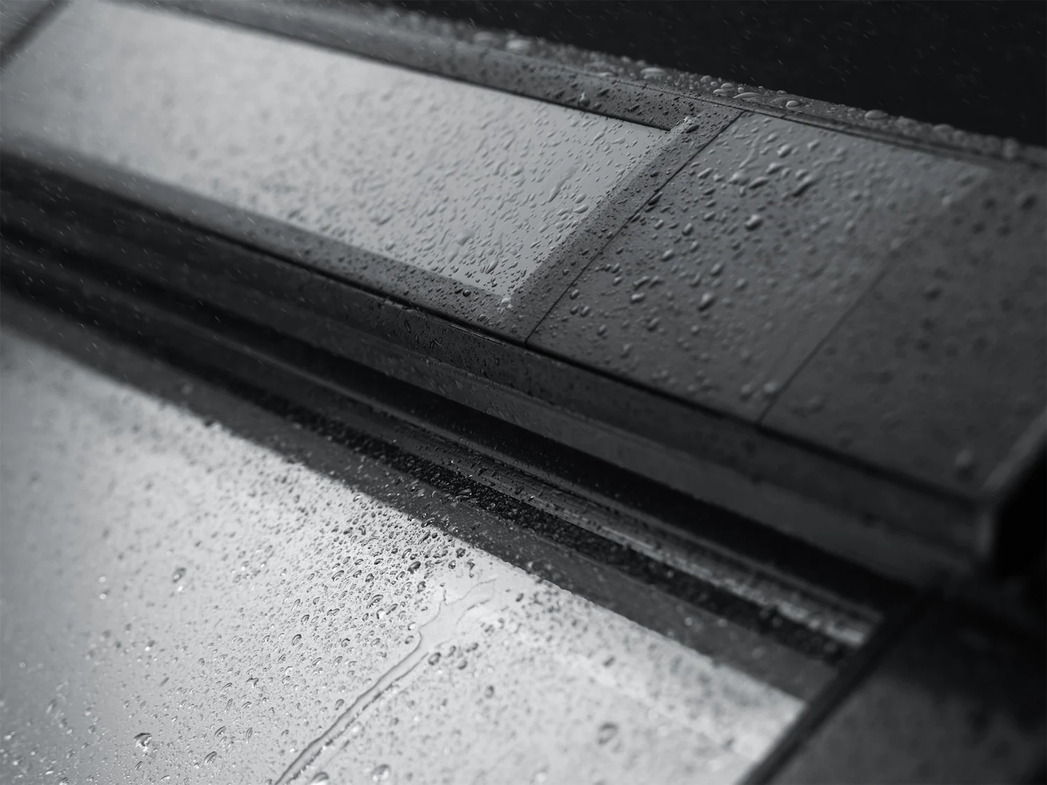 Gros plan sur des gouttes de pluie sur un panneau solaire Velux intégré à côté d'une fenêtre de toit, par temps pluvieux.